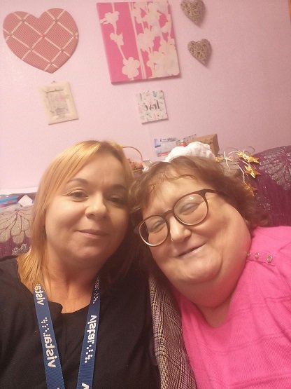 Mandy and a member of Vista’s deafblind service are sitting on a sofa and they are smiling together.