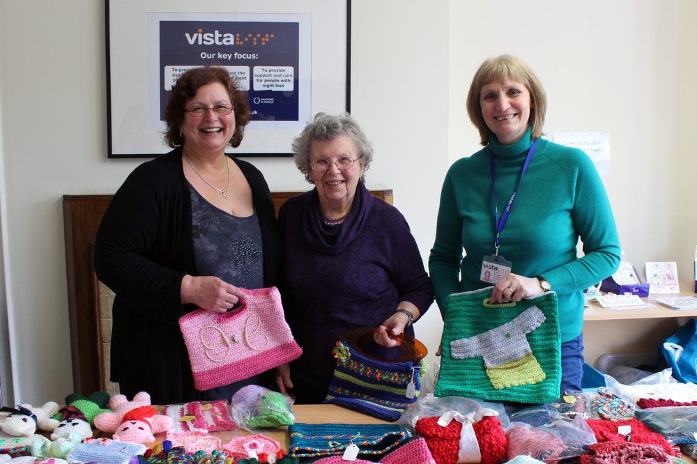 A picture of Sheila with Carol and Sue from Vista's befriending service, holding knitting bags at a fundraising sale.