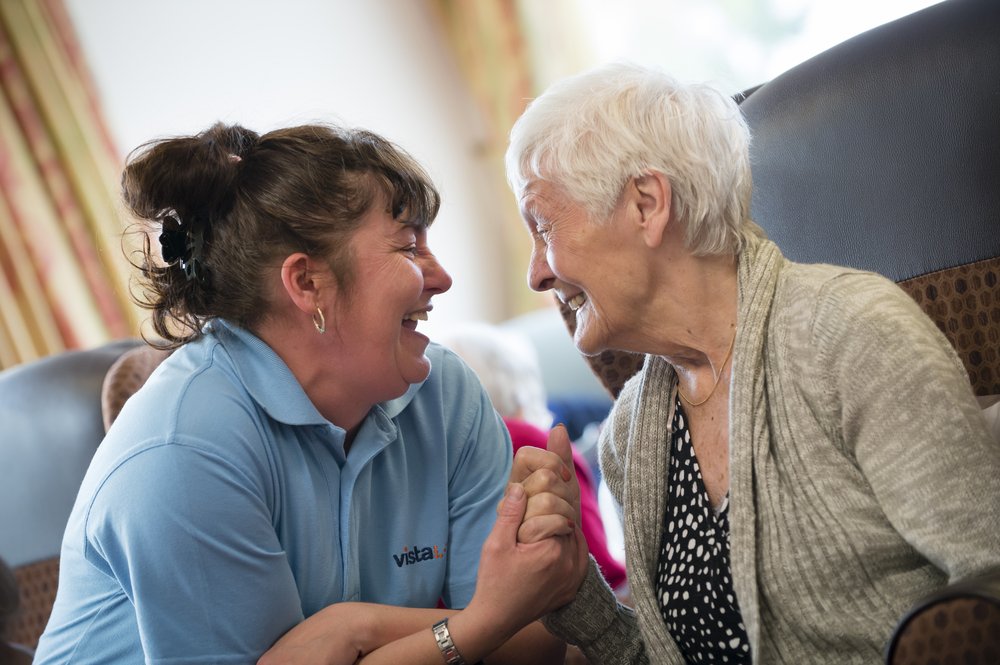 A picture of a Vista care assistant holding hands and smiling with a resident.
