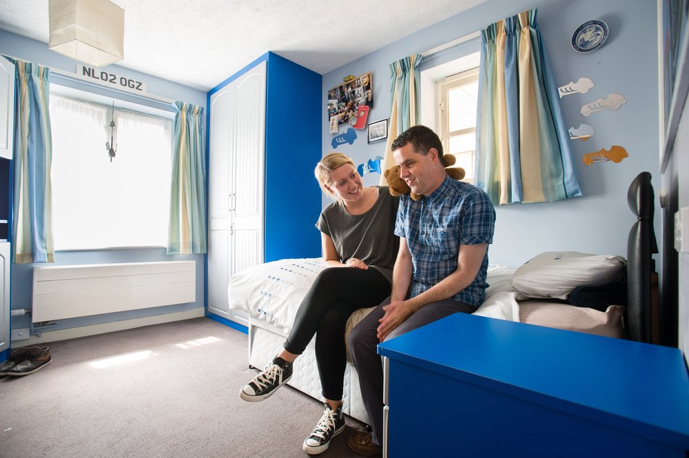 A picture of a staff member talking to a resident in his bedroom.