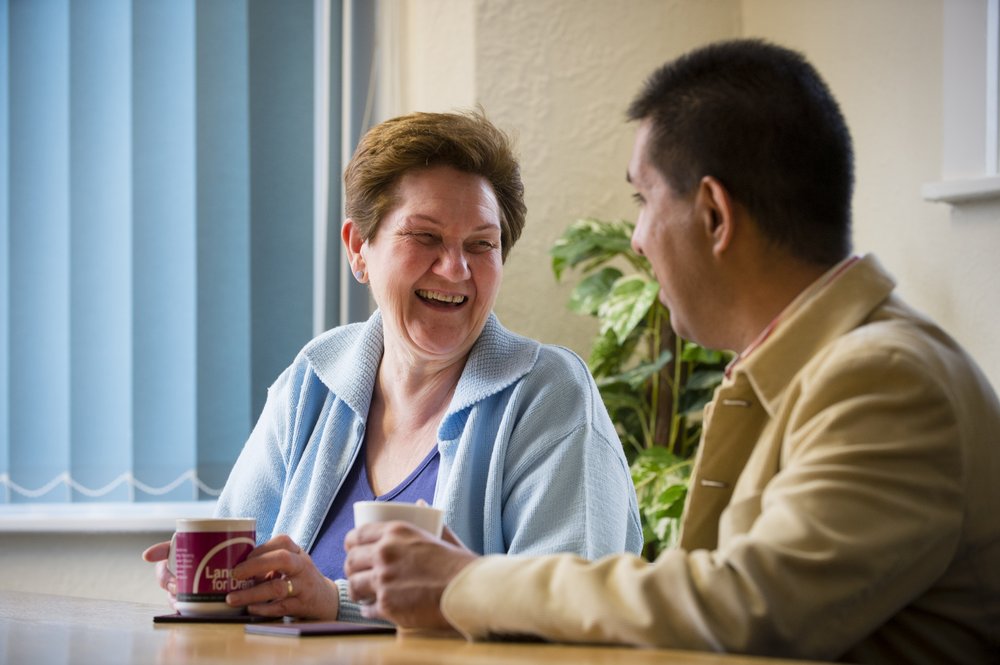A picture of a male befriender and female befriendee sitting down, having a coffee and a chat.