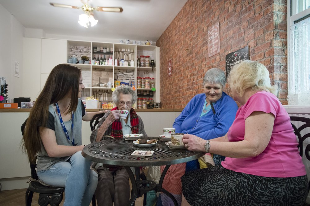 A picture of a staff member sat with residents in the home's cafe.