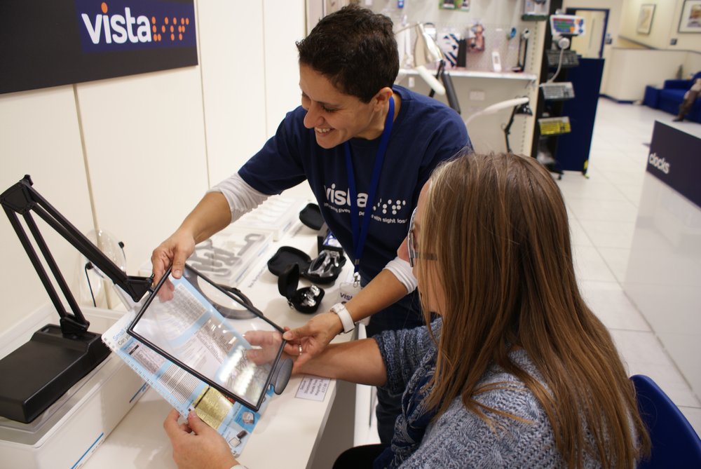 A picture of a shop volunteer demonstrating a magnifier to a customer.
