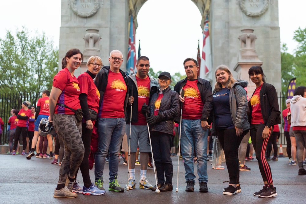 Group shot of 8 Vista runners, wearing Red Sunrise City t-shirts, standing in front of the war memorial in Victoria Park