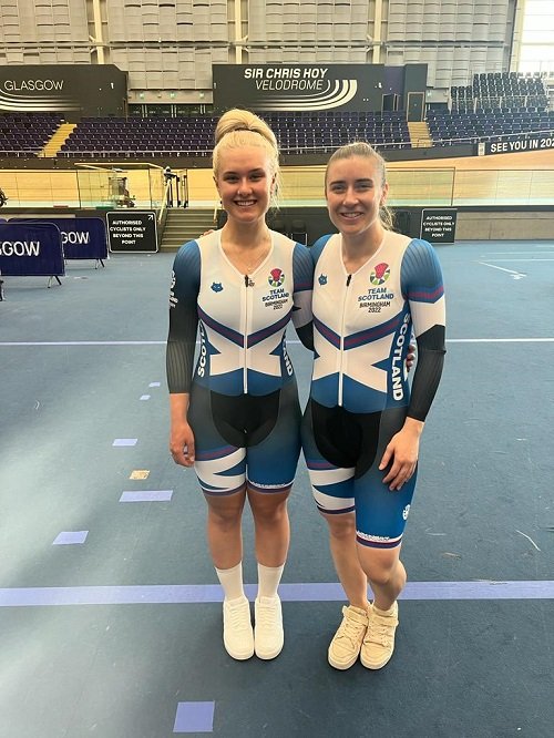 Jenny Holl and Libby Clegg in Team Scotland clothing standing smiling on the cycling track.