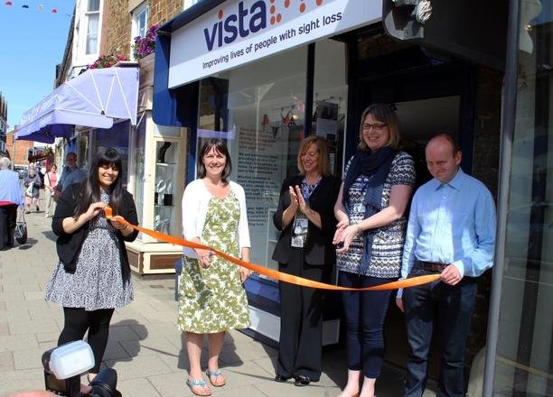 A picture of an orange ribbon being cut in front of the charity shop doors.
