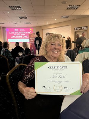 Julie Rudd holding a finalist certificate at this year's Care Professional of The Year Awards, 2022. She is grinning while she holds the certifcate.
