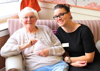 A carer with an older woman on a sofa, smiling away.