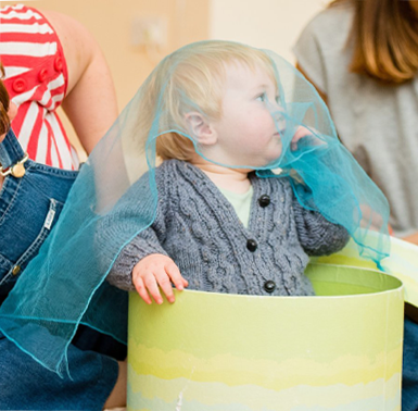 A picture of little child with blue fabric over their head, sat in a bucket