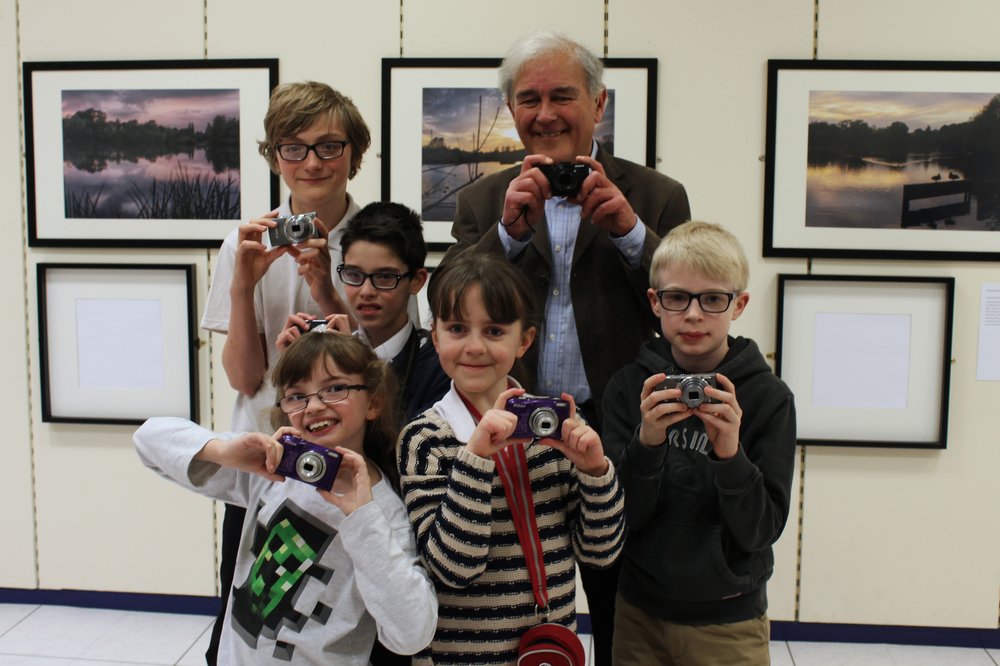A picture of Vista Ambassador Brian Negus with children and young people, all holding cameras.