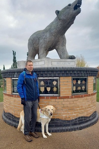 A man standing by a statue with a guide dog.