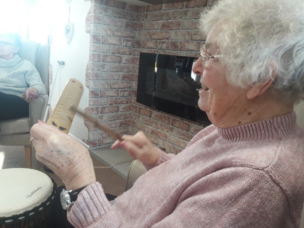 A lady playing a musical instrument at Vista's Kathleen Rutland Home as part of a warm days activity. She is smiling.