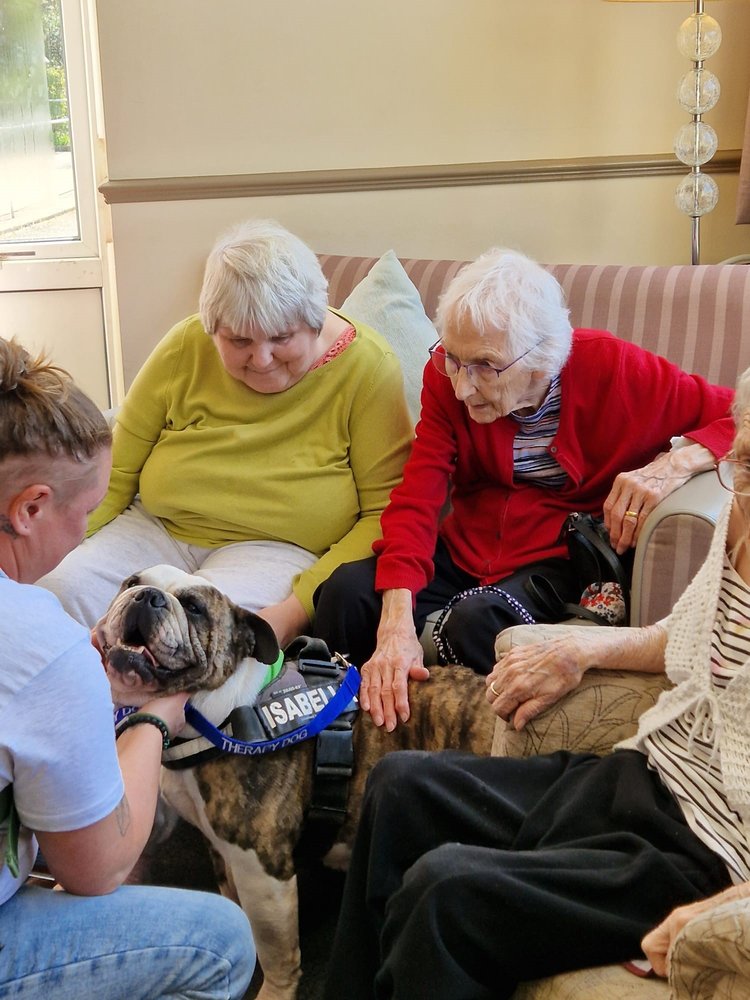 Three residents at Vista's Kathleen Rutland Home smiling on the sofa and stroking a dog.