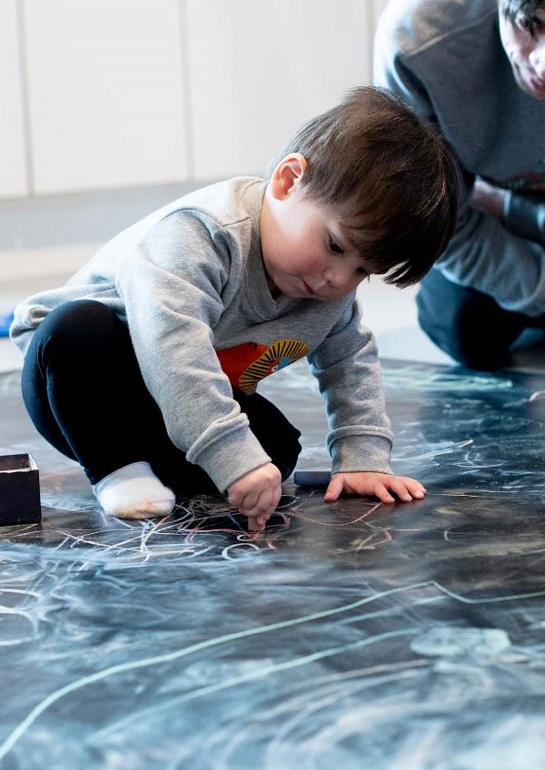 Image is of a child playing and colouring on a chalk board