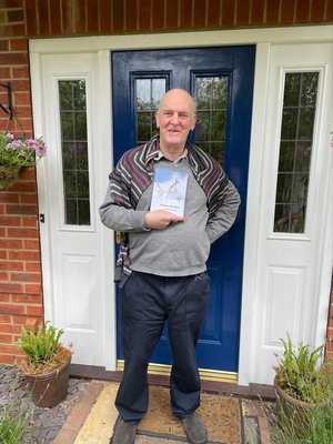 Alec Crombie is smiling and standing by a blue door holding his book 'Become the Wind'