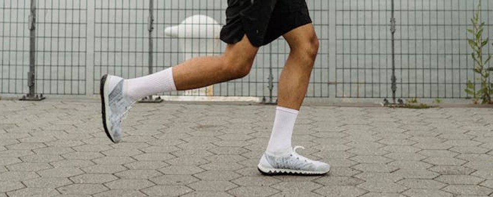 [Image Description: A man's legs in running trainers running along a pavement with water visible through a fence behind.]