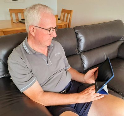 Vista's Tech Together volunteer, Chris is sat on a sofa and focused on a tablet.