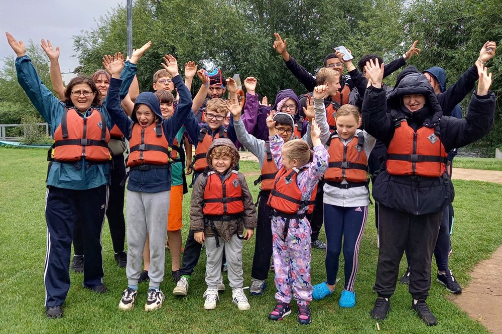 A group of children and young people stand with Vista members of staff wearing life jackets as a part of one of Vista's CYP activities.