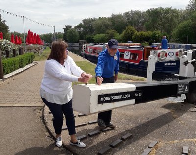 A woman in a white top helps a man in a blue coat to move a lock gate