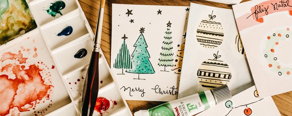 [Image Description: A collection of different christmas cards, pens and creative tools sit on a wooden table.]