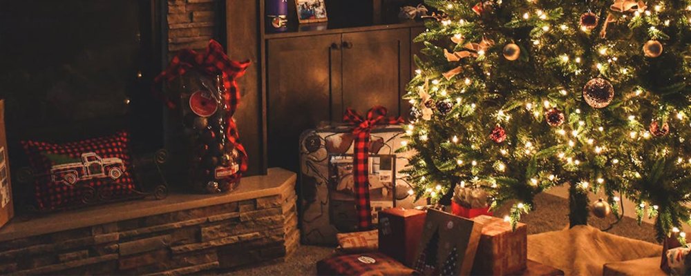 [Image Description: A decorated Christmas tree with glowing lights stands beside wrapped presents and festive décor in a cozy living room.]