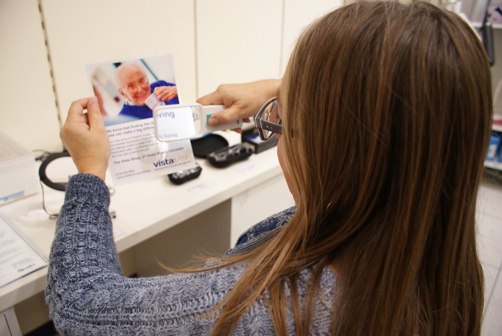 A picture of a lady using a magnifier to read a leaflet.