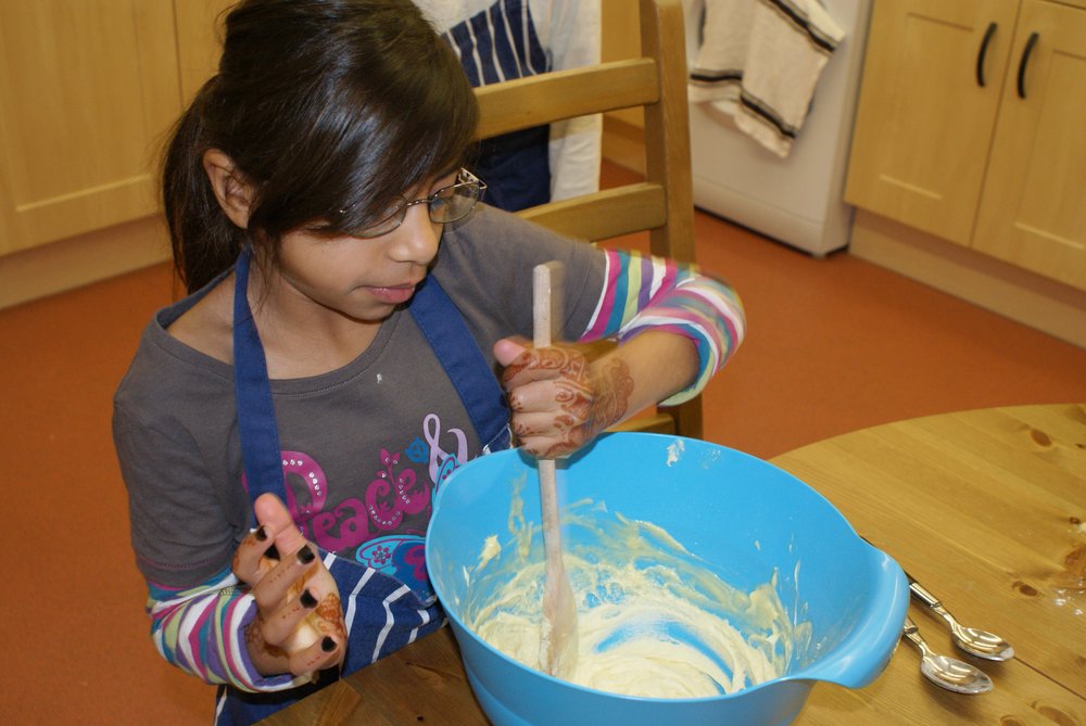 A picture of a young girl stirring ingredients with a wooden spoon in a blue mixing bowl.