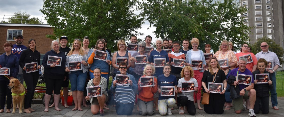 Image is of everyone who took part in Vista's firewalk holding their certificates at Loughborough University, Shirley Pearce Square and they are all smiling after completing the challenge.