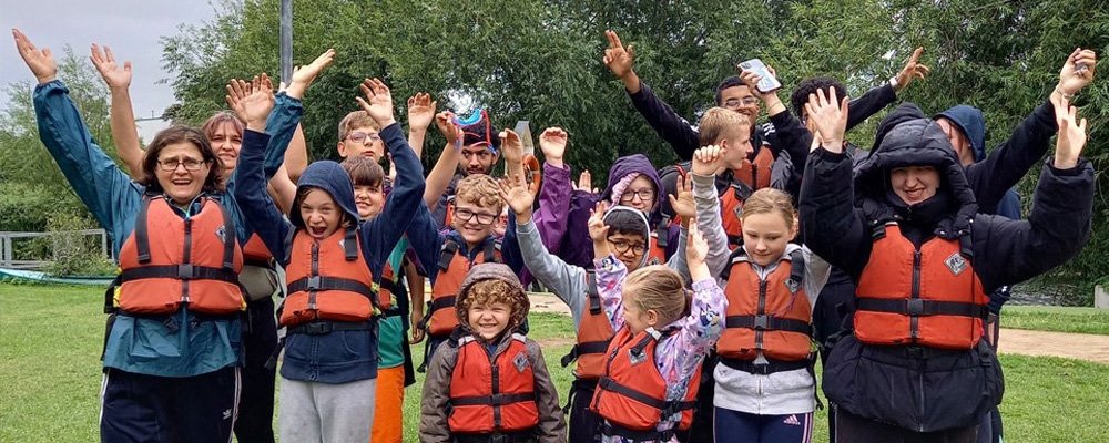 [Image Description: A group of children and young people stand with Vista members of staff wearing life jackets as a part of one of Vista's children and young people activities.]