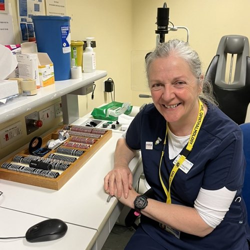 Doctor Jane Macnaughton sat wearing her NHS uniform with the various equipment and tools an Optometrist uses surrounding her.