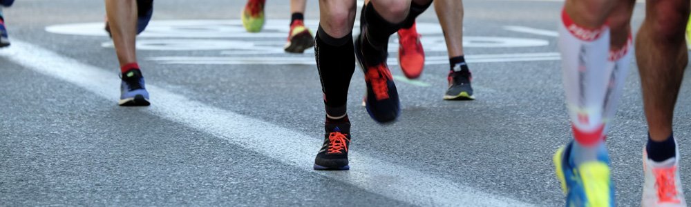 [Image Description: Several feet in trainers running along a concrete road in a marathon.]