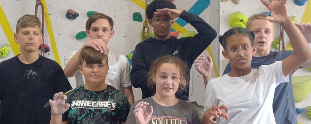 [Image Description: Group of children posing together in front of an indoor climbing wall.]