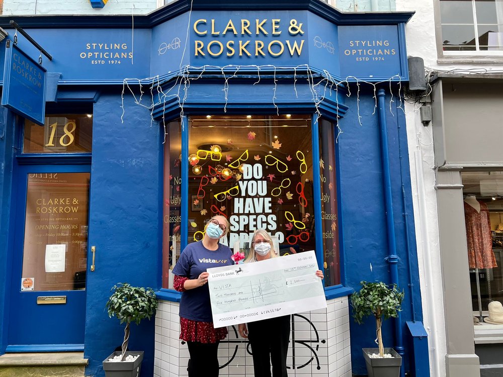 Image is of Amanda, Vista's Corporate Fundraiser receiving the cheque for £2,500 outside Clarke and Roskrow Styling Opticians in Market Harborough.