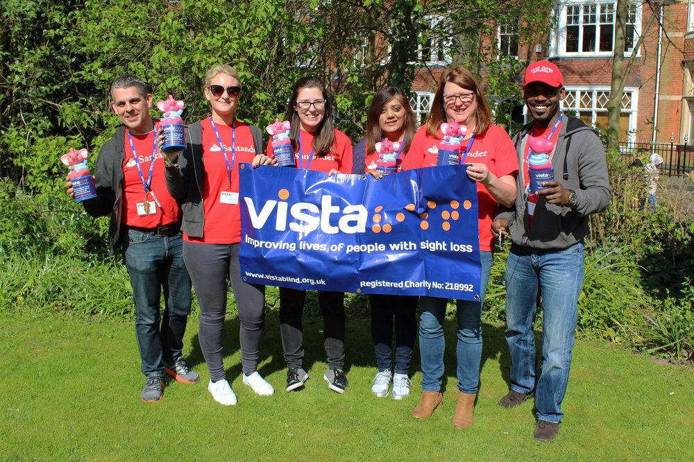 A picture of the Santander team holding collection boxes and a Vista banner.