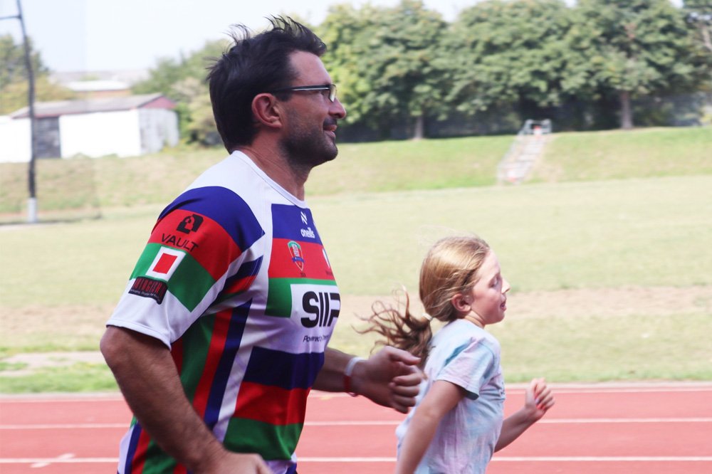 A man and his daughter run along a running track together.