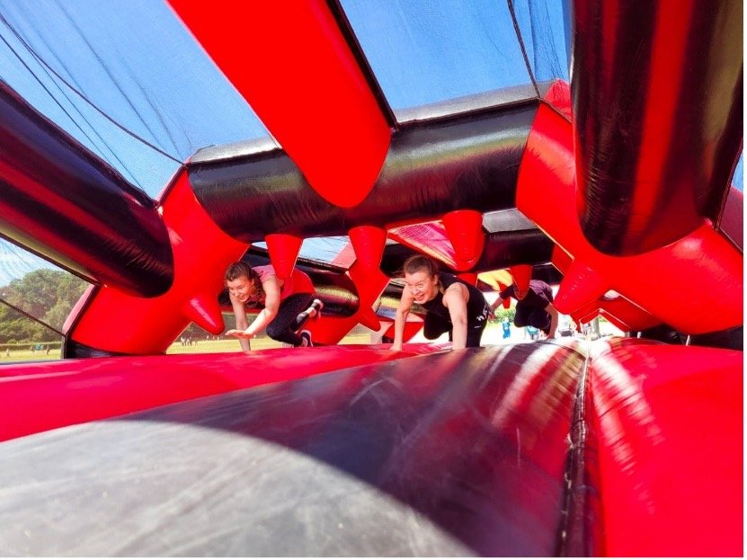 Image description: Two men smiling crawl through a large red inflatable obstacle course.