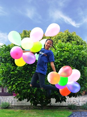 Amelia in a Vista t-shirt holding a bunch of balloons in each hand as she jumps.