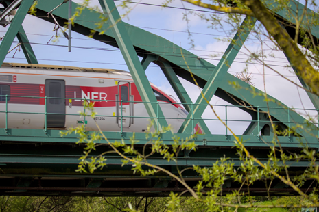 [Image of an LNER Train going across a railway bridge. Plants and shrubbery surround the bridge.]