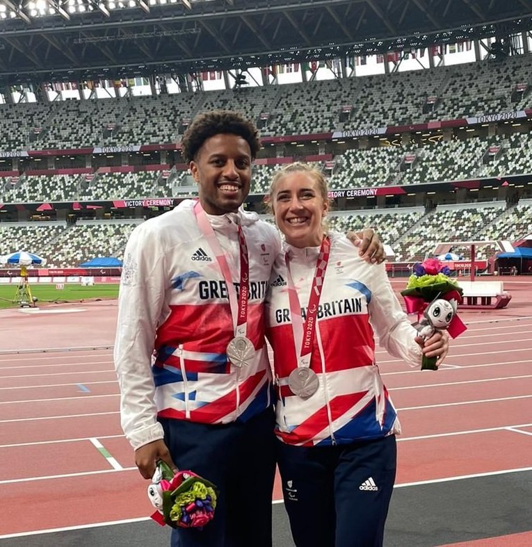 Image is of Chris Clarke and Libby Clegg in Great Britain tops holding flowers and standing on a running track.