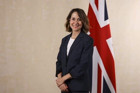 [Image Description: Image of Liz Kendall stood in front of a Union Jack Flag. Image sourced from GOV.UK.]