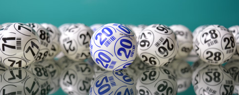 [Image Description: An assortment of lottery balls are visible on a mirrored table. The numbers 71, 20, 26 and 28 are visible on some of the balls, with the rest being blurred.]
