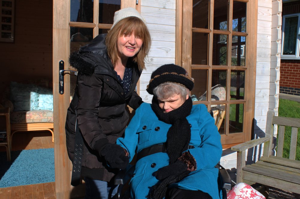 A picture of Maggie and Bridget sat outside in the garden together, holding hands.