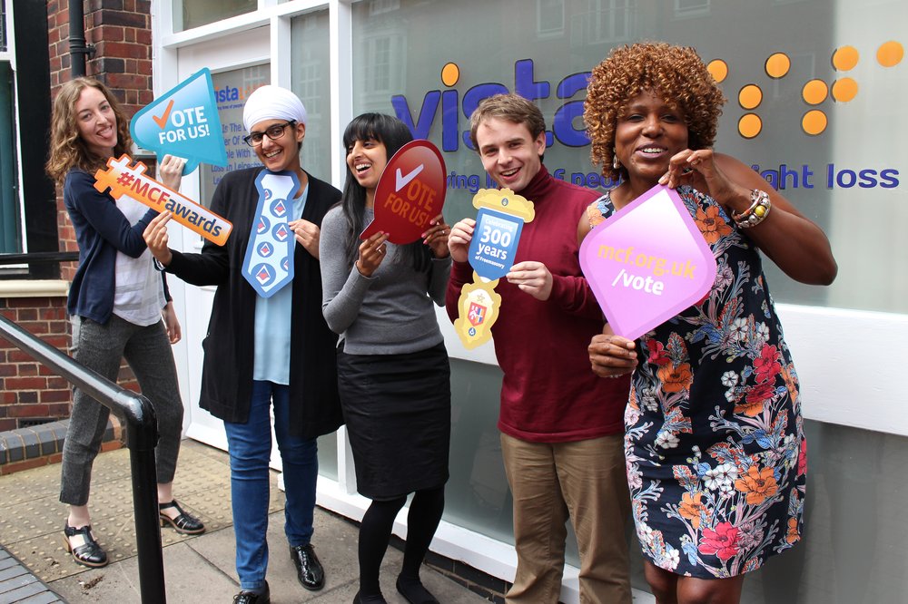 A picture of Vista staff holding voting competition signs.