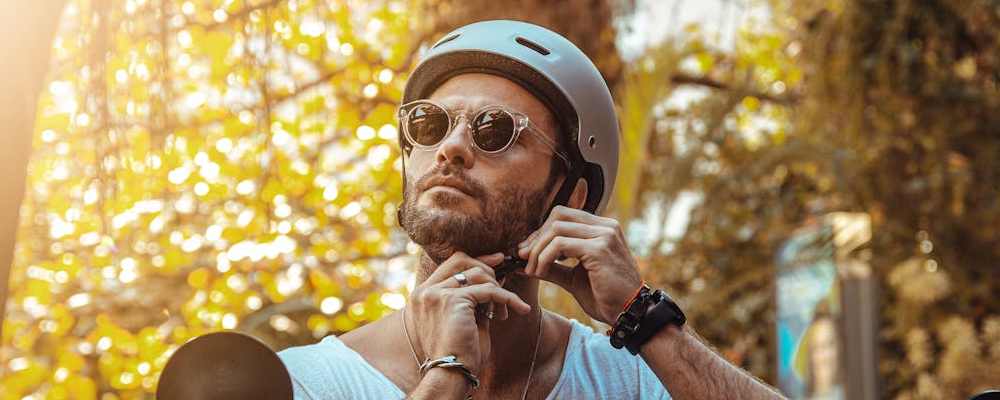 [Image Description: An image of a man on a scooter wearing a helmet and a pair of sunglasses. Trees and sunshine can be seen behind him.]