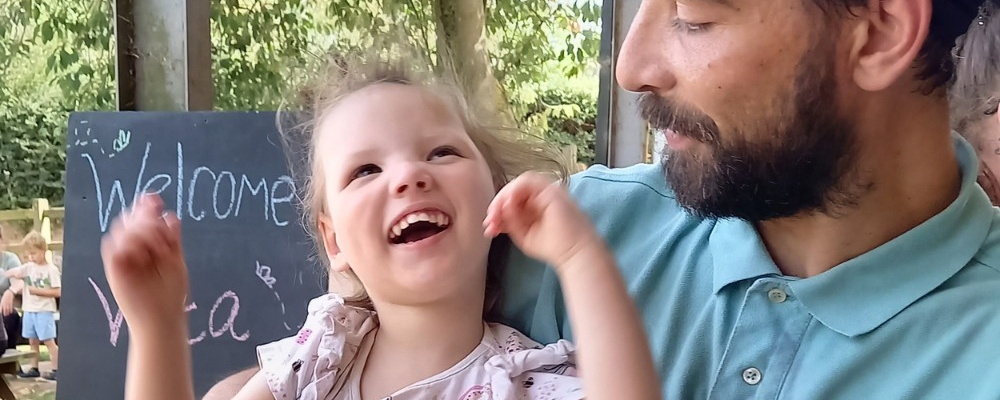 [Image Description: A dad holds his daughter on his lap. She is laughing with joy while looking up at him.]