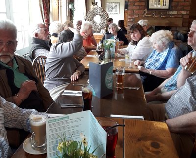 The group of 16 people say around a large pub restaurant table, with menus and flowers on the middle