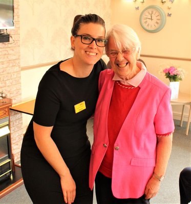 Hayley Barr, in a black dress, with her arm around a resident in a pink blazer