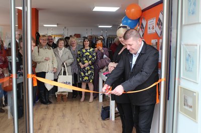 The ribbon across the door is cut by a man, a large audience clapping along