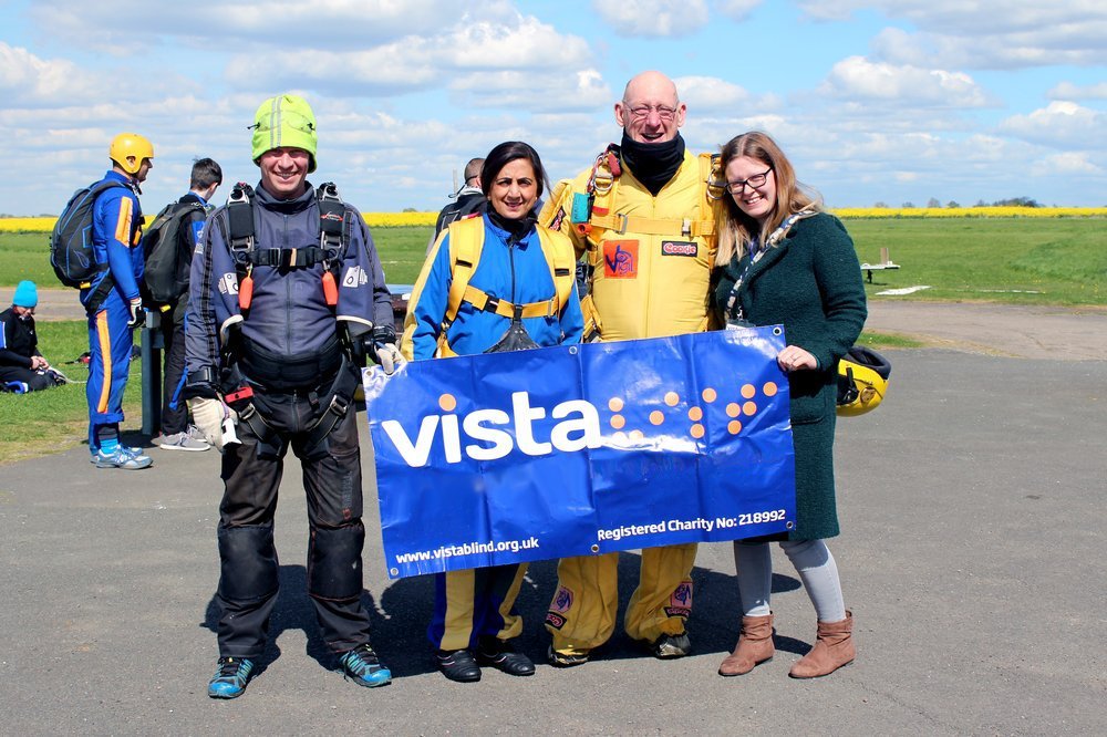Team Vista in skydiving equipment holding a 'Vista' banner.