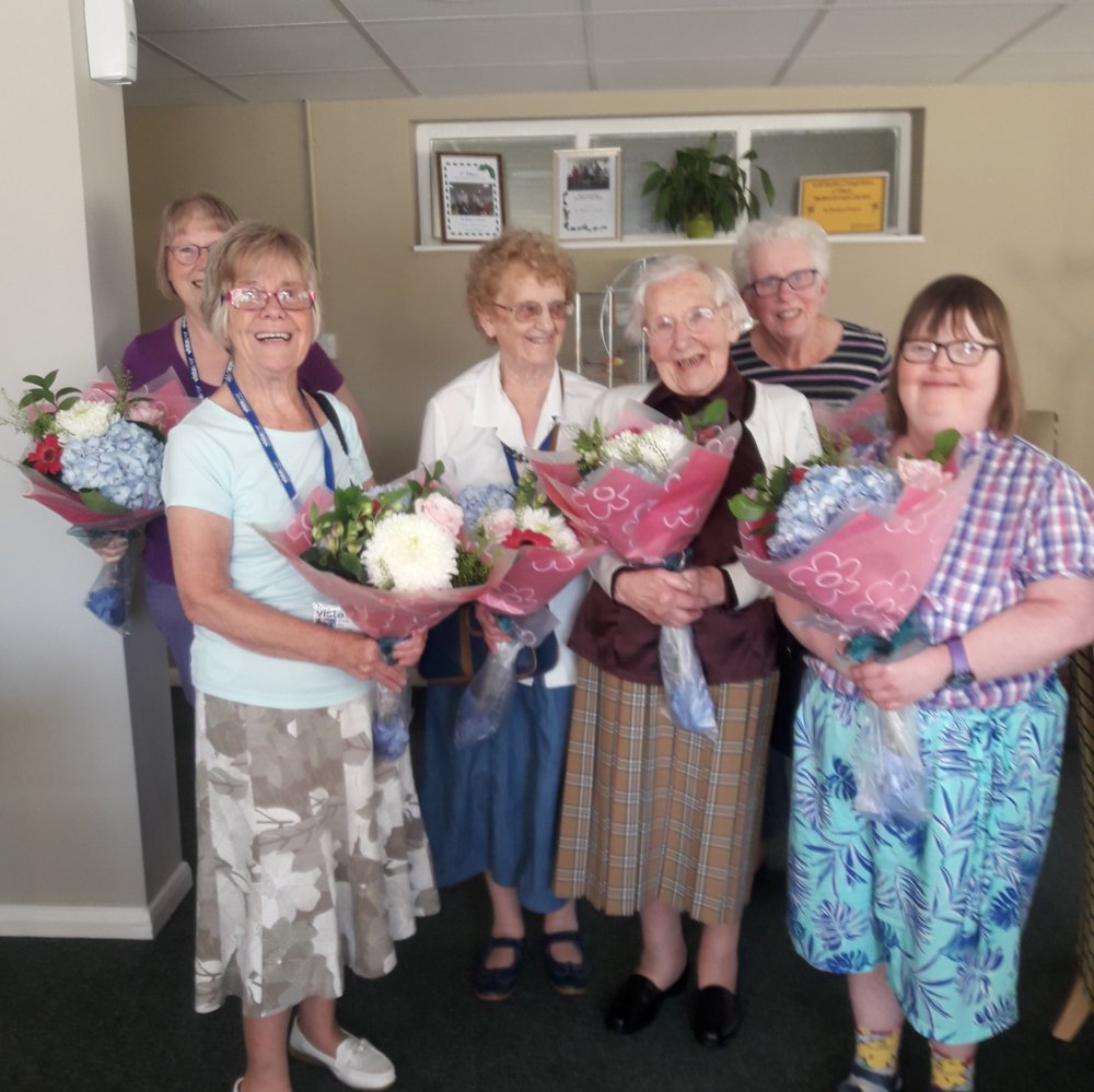 5 volunteers stood in a line, holding flowers they've recieved